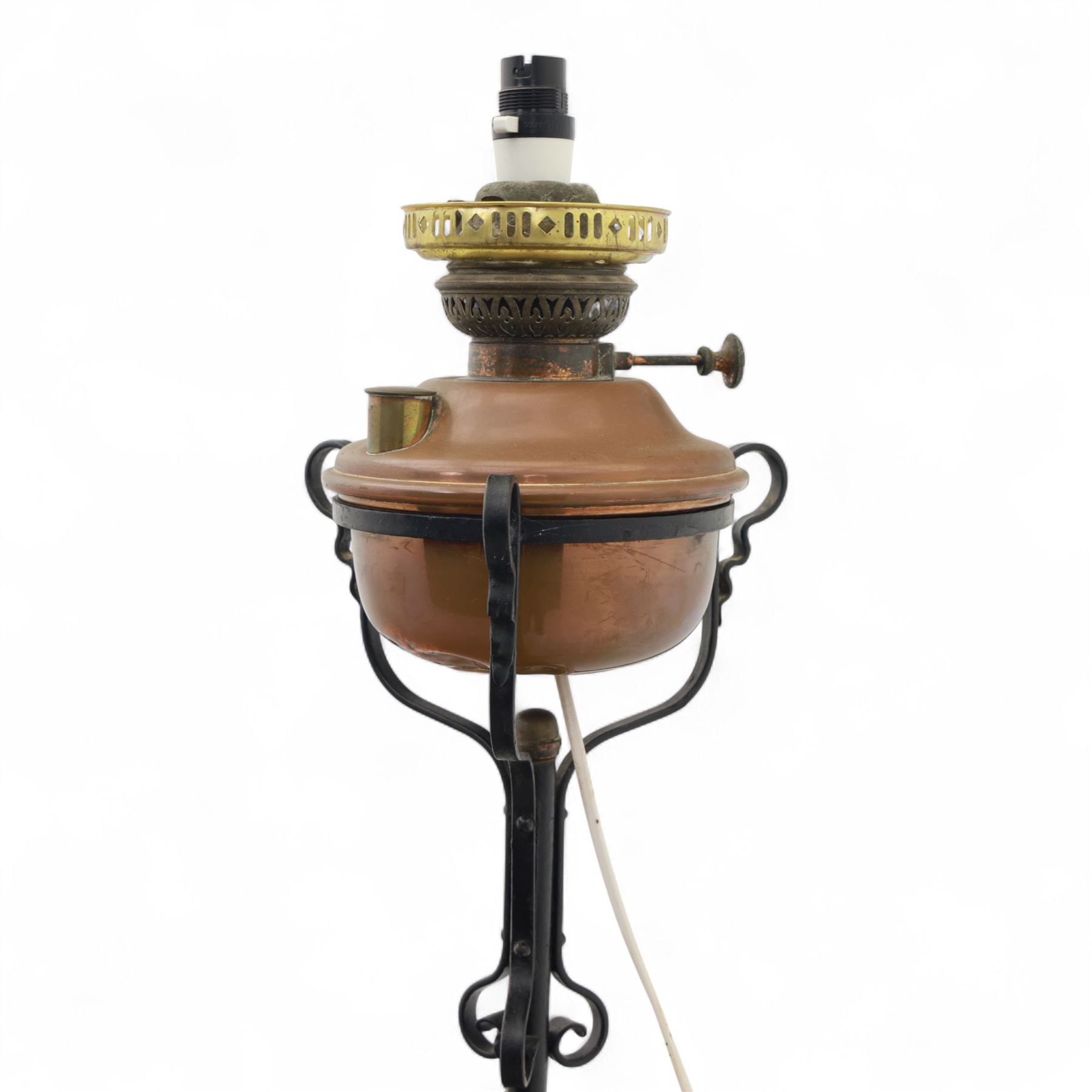 Early 20th century converted oil lamp standard, with copper reservoir and brass burner mount, later wired for electricity, on wrought iron tripod stand with scroll and twist ornamentation