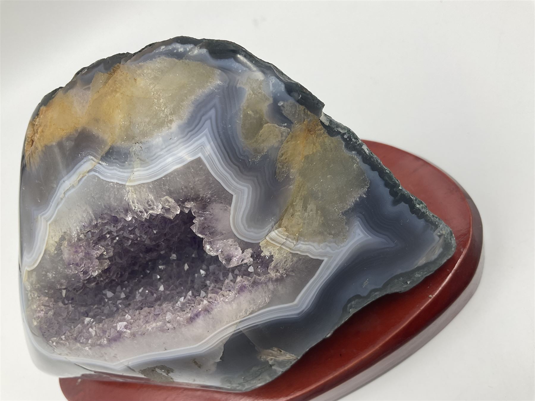 Amethyst crystal geode cluster, with well-defined crystals of various sizes, upon a carved wooden stand, H12cm, L20cm