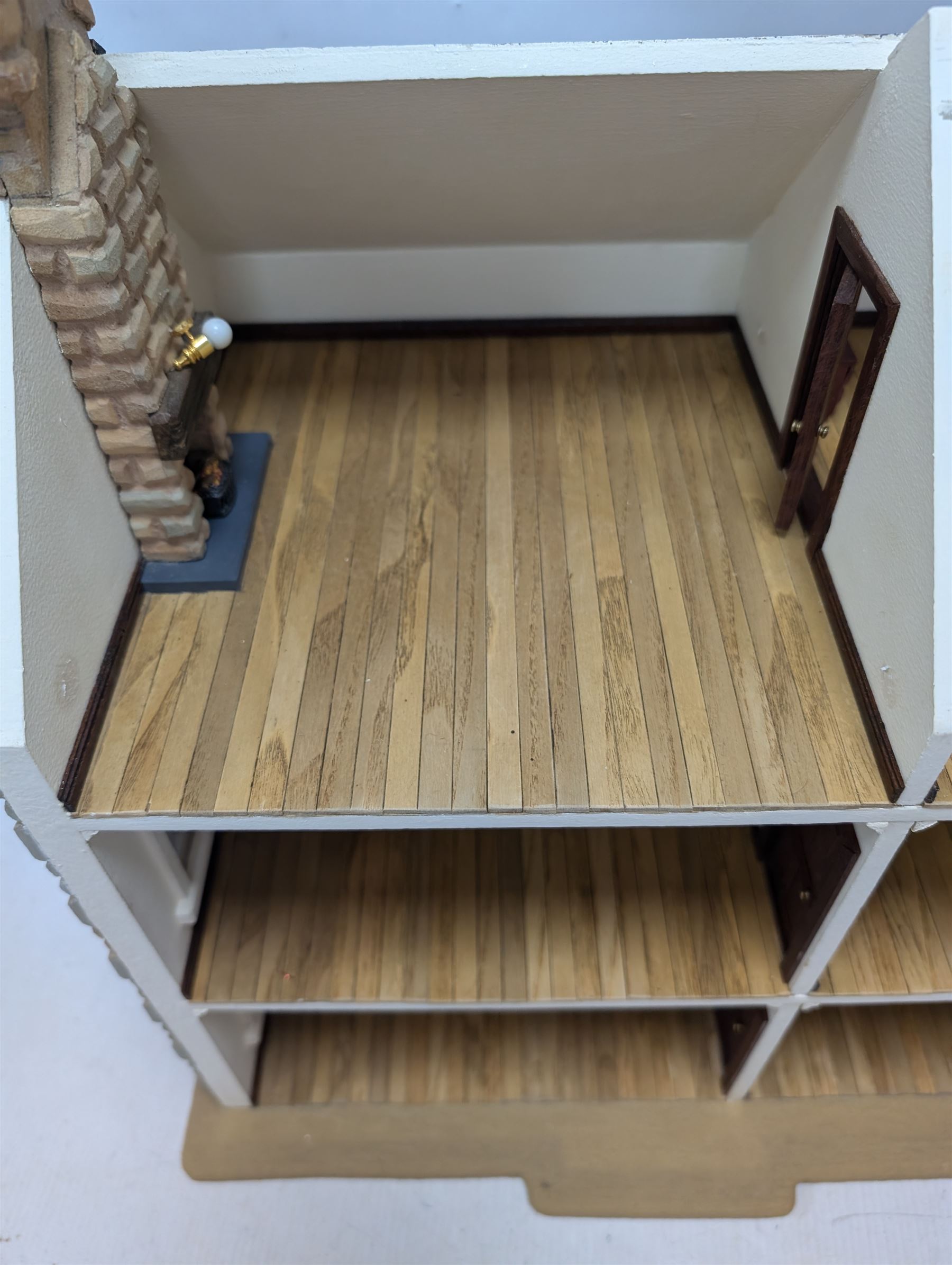 1:24 scale stone effect three-storey cottage dolls house, with green arched door and lattice effect windows, decorated to the interior with wooden floors, wired lighting and fire places, H45cm, W57cm, D26cm