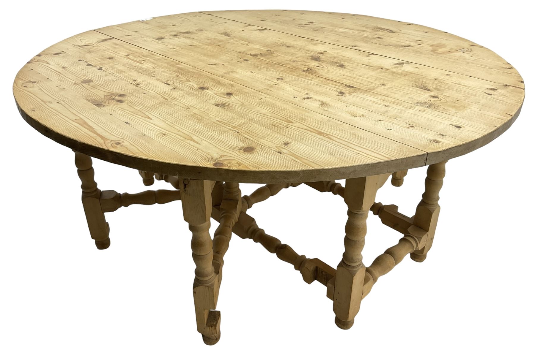 Traditional stripped pine dining table, circular drop-leaf top over double gate-leg action base with turned supports united by turned stretchers