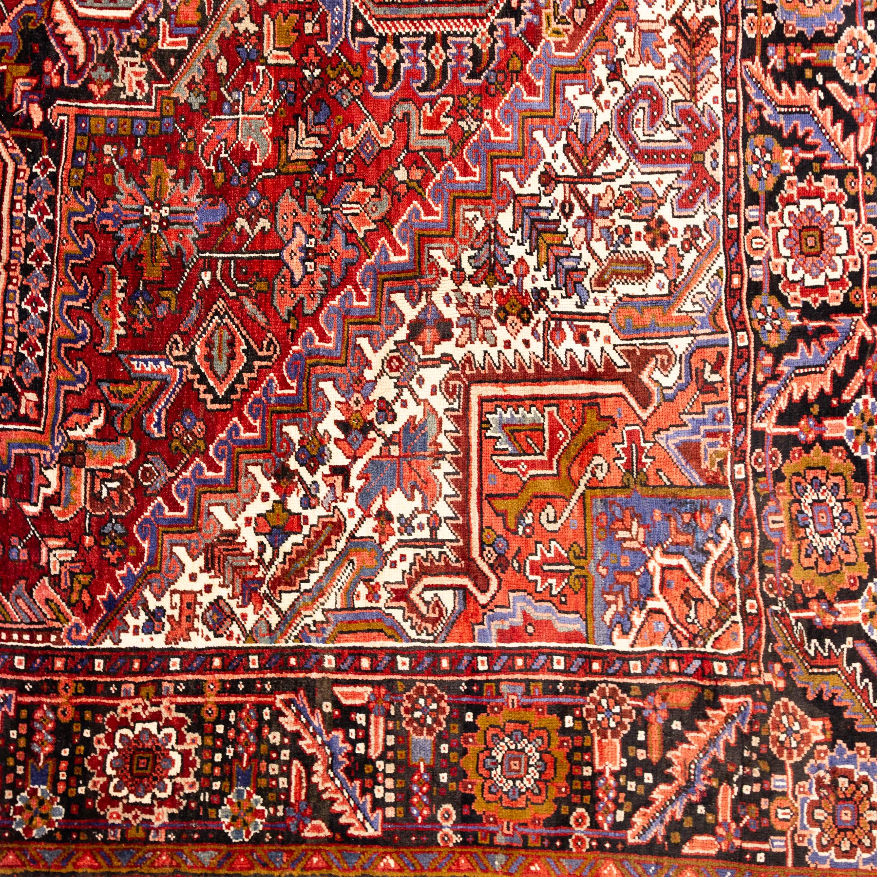 North West Persian Heriz hand-knotted carpet, brick red field, with large central angular star medallion with stepped outlines, surrounded by geometric floral devices and stylized rosettes, with corresponding corner spandrels, enclosed by a bold geometric main border with multiple guard stripes, with cotton fringe ends 