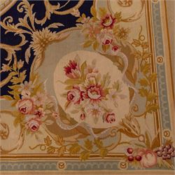 20th-century Aubusson-style woven tapestry wall hanging of rectangular form, the design with a central oval floral medallion composed of delicate sprays in soft pinks, creams, and muted green enclosed by an elaborate dark blue scrolling acanthus ground enriched with foliate ornamentation, field framed by floral cartouches to the corners and multiple guard borders in pale blue, ivory, and ochre tones