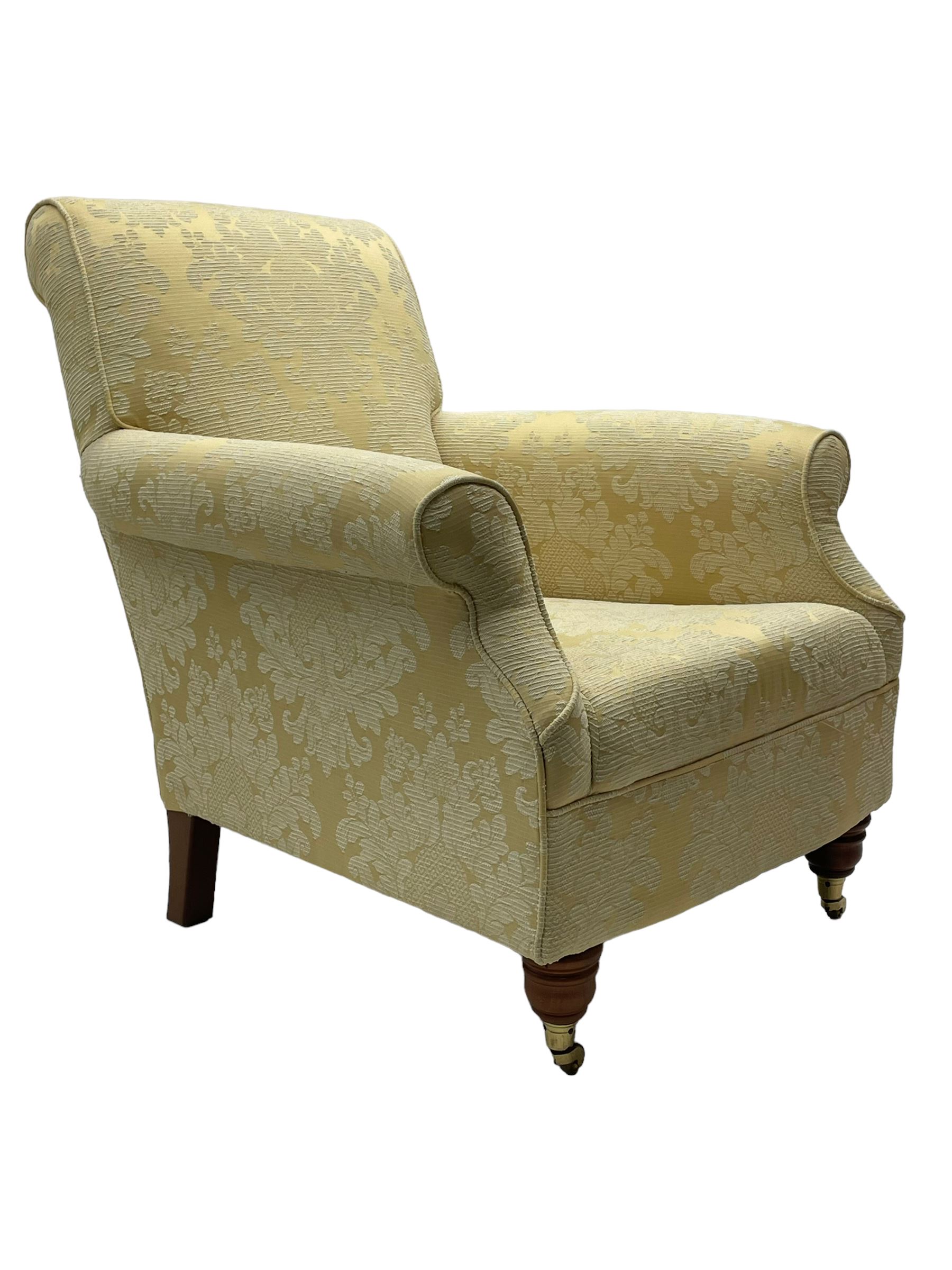 Traditionally shaped hardwood-framed armchair, rolled back and arms, upholstered in pale gold and cream damask fabric with repeating foliate pattern, on turned feet with brass cups and castors