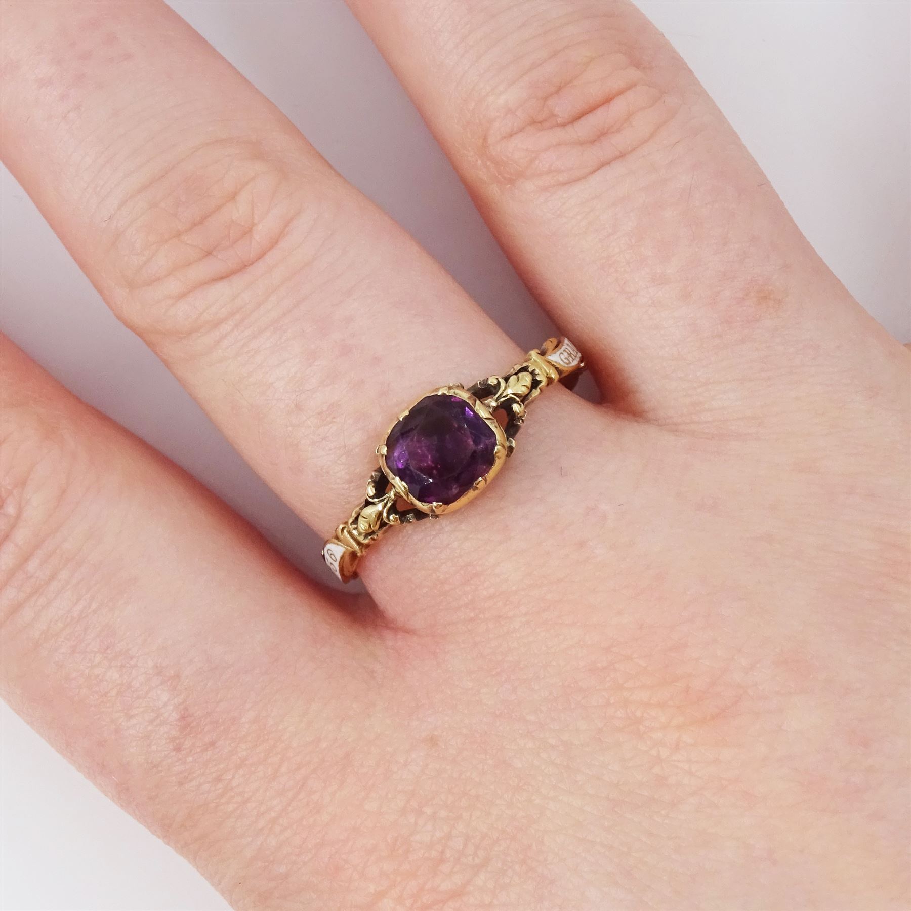 George II 18ct gold amethyst and enamel mourning ring, single cushion cut amethyst, with foiled and glazed back, to pierced fleur-de-lis shoulders, the white enamelled shank engraved Grace Hutchinson OB: 13 Dec: 1756