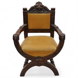 Victorian heavily carved oak X-framed throne chair, the cresting rail carved with mask and curling foliage, upholstered in mustard fabric, the arms and frame carved with scrolling foliage, united by turned stretchers 