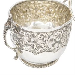 Late Victorian silver twin handled sugar bowl, profusely embossed with floral and scrolling decoration and acanthus capped handles, upon stepped oval base, hallmarked Josiah Williams & Co, London 1897, together with a Victorian twin handled sugar bowl, of circular form with embossed and chased foliate decoration and seated figures capping each handle, upon circular base, hallmarked London 1888, maker's mark indistinct, tallest H11cm
