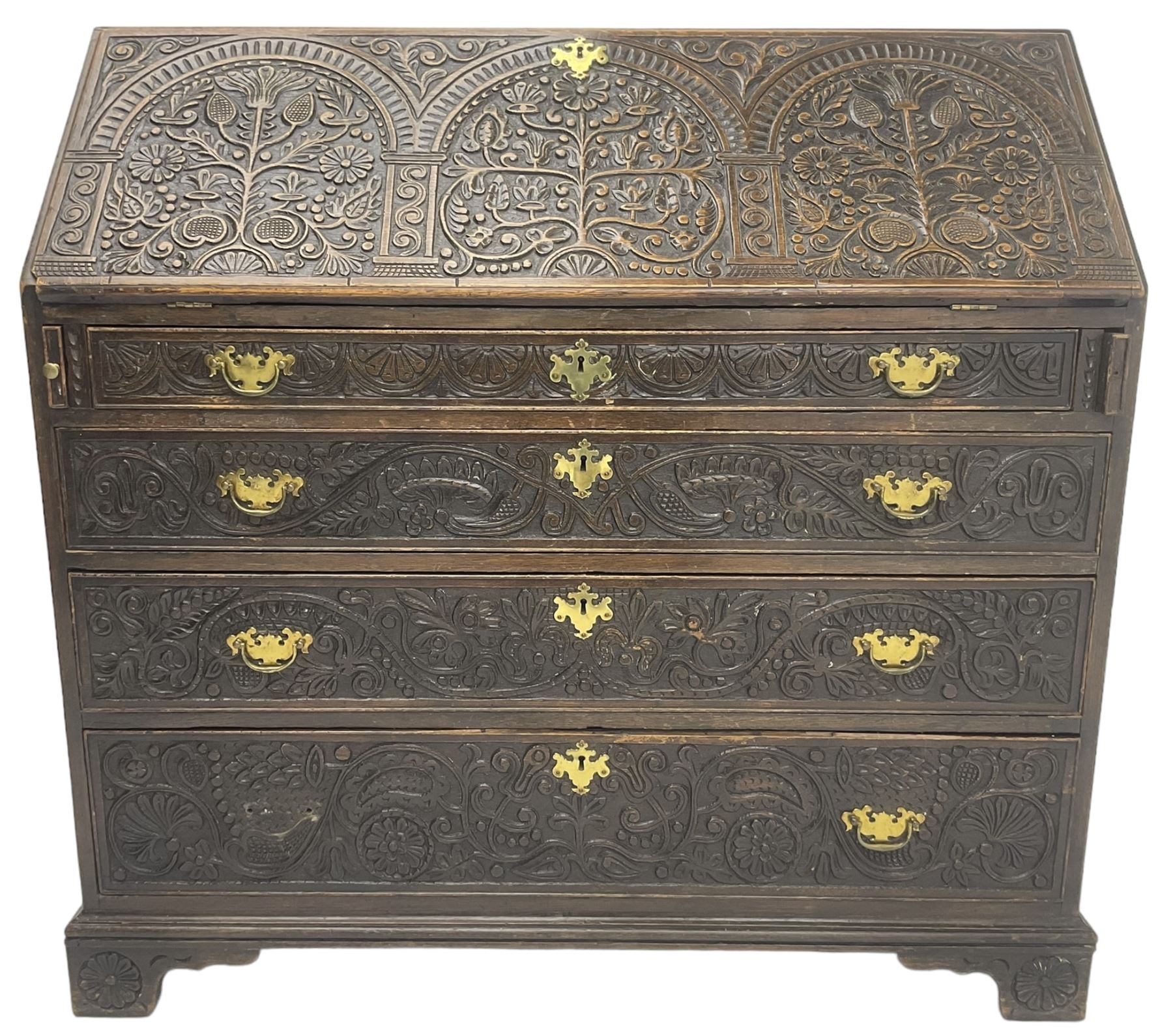 18th century heavily carved oak bureau, the fall front relief carved with three arches enclosing plants and flower head decoration, the interior fitted with pigeonholes, drawers and cupboard, four graduating cock-beaded drawers below, carved with lunettes and trailing foliage decoration, on bracket feet