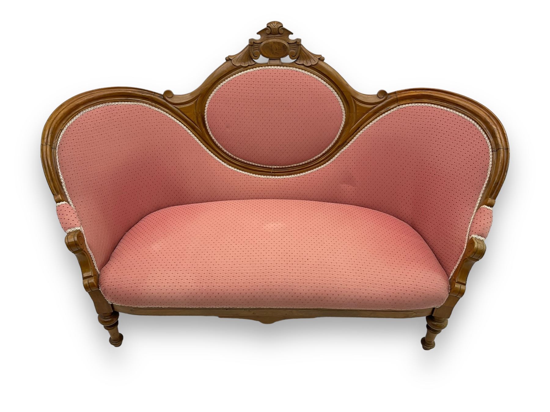 Late Victorian walnut framed double spoon back sofa, shaped crest rail with central carved medallion over curved back with pink upholstery, scrolling arms with additional carvings, on turned supports