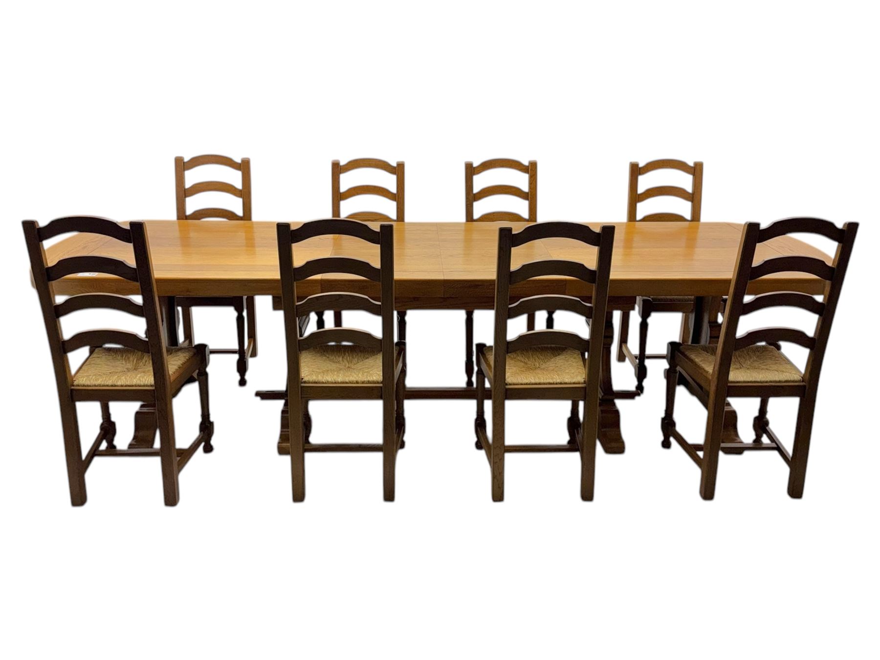Oak extending dining table with elegant scrolled shaped double pedestal base and scrolled feet; together with a set of eight ladder back chairs with rush seats ((9) table closed 228x95x79cm chairs 106x38x44cm 