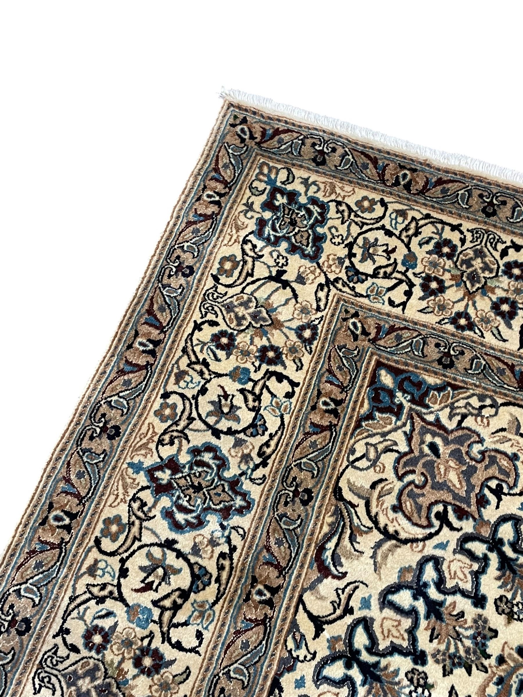 Persian Kashan ivory ground carpet, central rosette medallion surrounded by swirling leafy branches and floral sprays, the main border with scrolling pattern interspersed with floral motifs, within guard stripes 