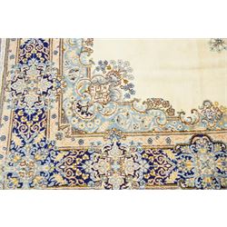 South East Persian Kirman hand-knotted carpet, ivory field with central floral medallion in tones of cobalt and pale blue, issuing scrolling vinery and palmettes, conforming spandrels, main border with scrolling foliage and stylized palmettes, framed by multiple guard borders, with cotton fringe ends 