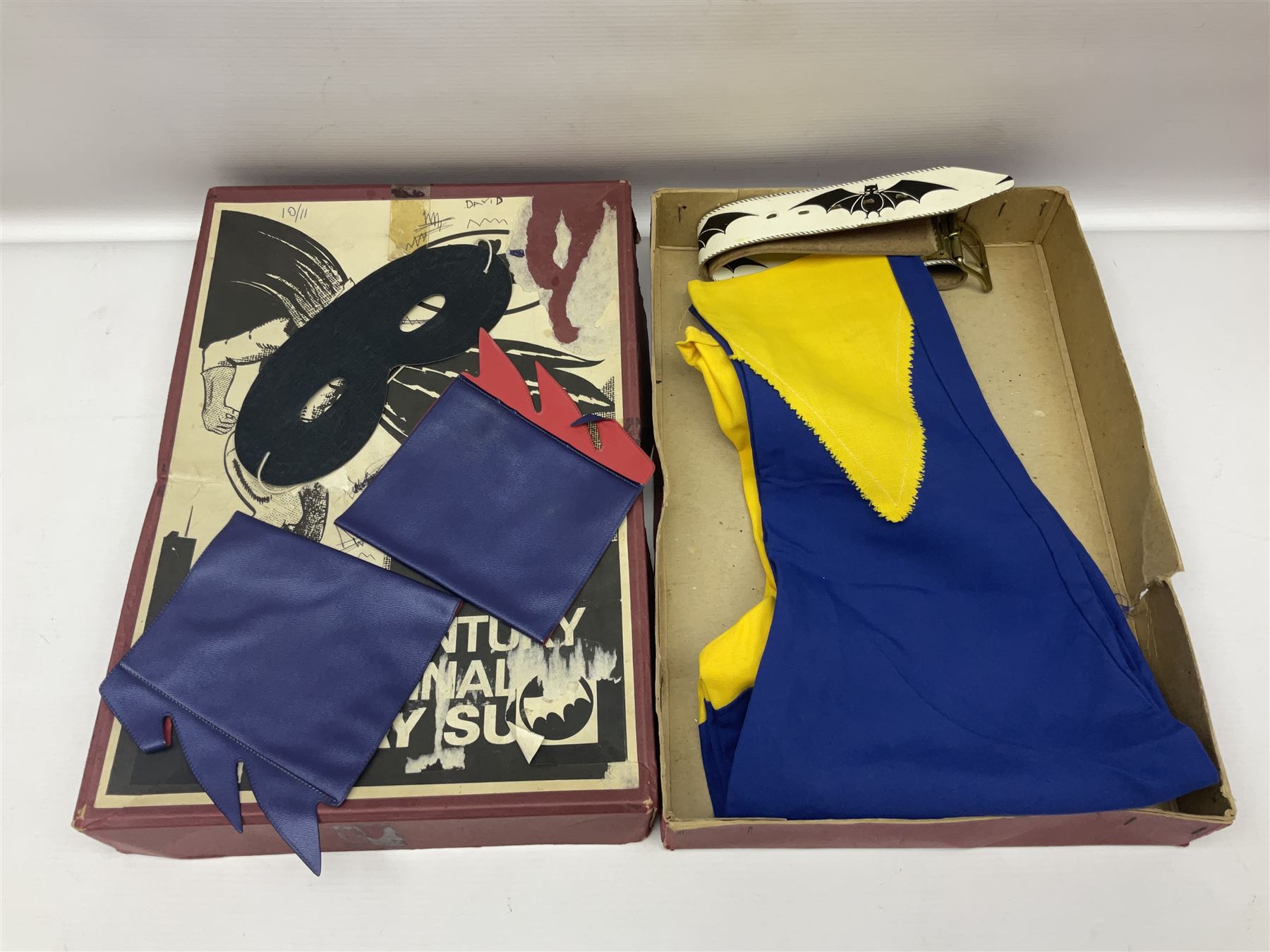 Two Boxed Batman Playsuit Costumes - 1960s 20th Century Original Play Suit, black eye mask, plastic vinyl cape/gauntlets, leather style belt, blue/yellow shirt, with Bat motif and blue/yellow pants; in original illustrated lidded box; and 1976 Decker Batman Playsuit costume, vinyl cape/ mask/gloves/boot tops/yellow belt, grey cloth top and pants; in original illustrated box (2)