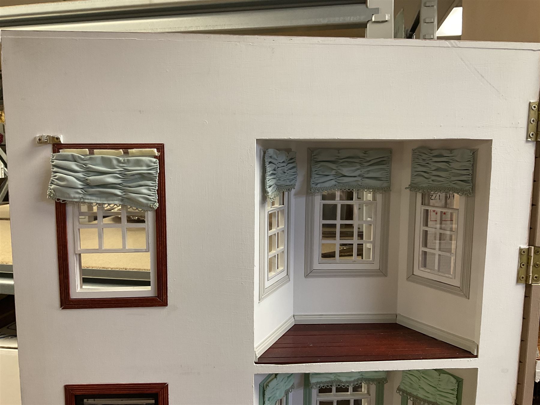 'The Hollies' - good quality sectional wooden doll's house in the form of a Georgian style four-storey bay windowed town house with simulated brick front elevation, rendered sides, off-set corner stonework, faux slate-hung top floor with flat roof and chimney stack, working sash windows, iron railings around front basement courtyard with hinged front elevation to two rooms with  spiral staircase, side hinged central section approached by external steps with iron balustrades to the sides leading to a front door, entrance hall with stairs to landing and two rooms on two floors with dado panelling and fire-surrounds, the top floor with top hung front elevation revealing stairs to a landing and bedroom; wired for electricity L51cm D65cm H107cm including chimney; together with a good quantity of quality wooden furniture and accessories including piano, dressers, bookcase and books, rugs, double half-tester bed, metalware, pictures etc