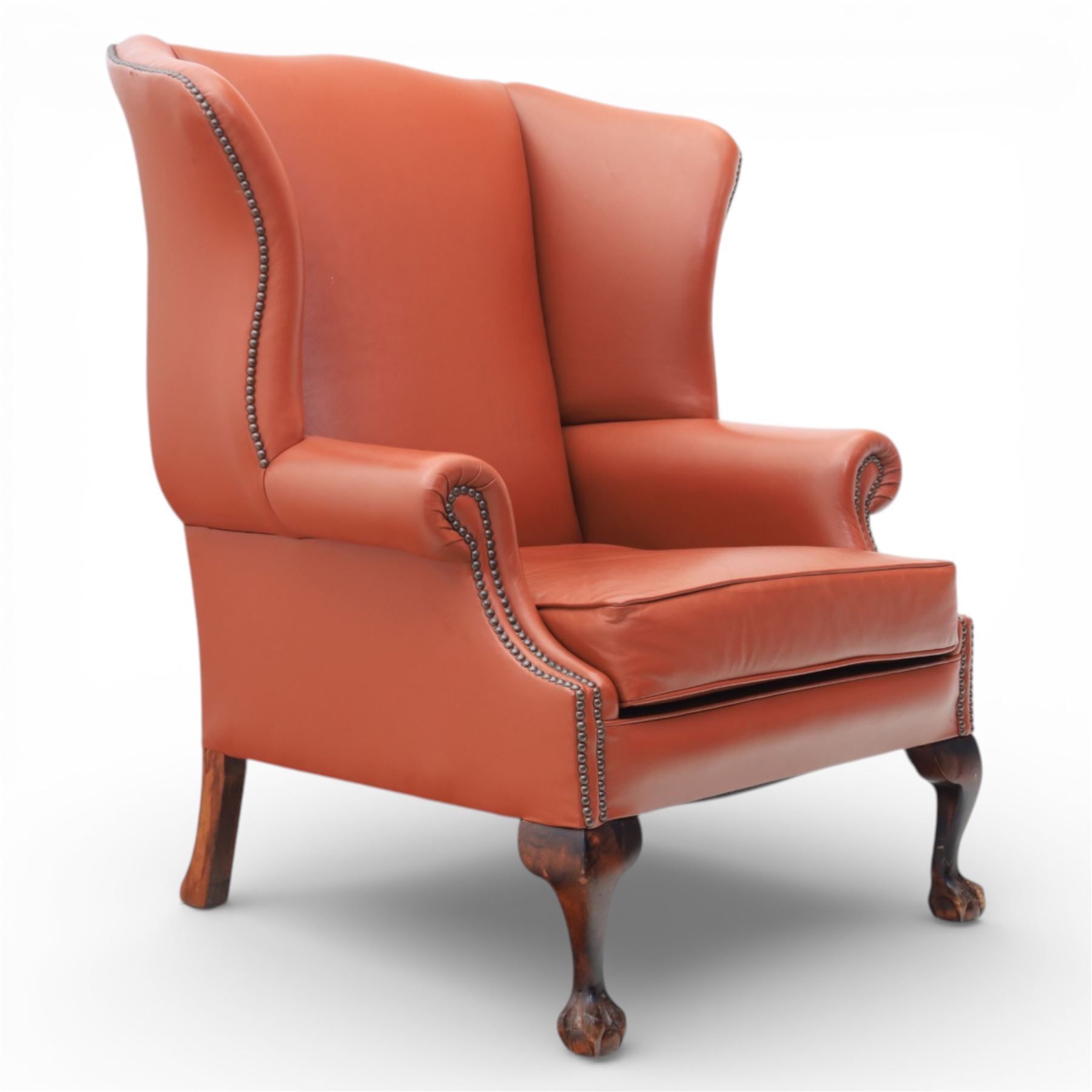 Georgian design red leather wingback armchair, with shaped back and scrolled arms, and close brass studded trim, upon cabriole front legs with claw and ball feet