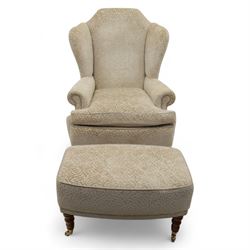 Late 20th century wingback armchair and matching footstool, upholstered in beige embossed fabric with brass stud edging, on cabriole legs and splayed rear legs, together with a matching footstool on turned supports terminating in brass castors (Stool H 42cm, W 75cm, D 47cm)