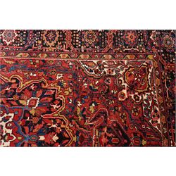 North West Persian Heriz/Ahar hand-knotted carpet, brick-red field with a large central angular stepped medallion with pendant motifs, surrounded by stylized palmettes, serrated leaves and geometric floral devices , ivory corner spandrels, enclosed by a dark indigo main border of stylized rosettes and angular vine motifs, between multiple guard stripes, with cotton fringe ends 