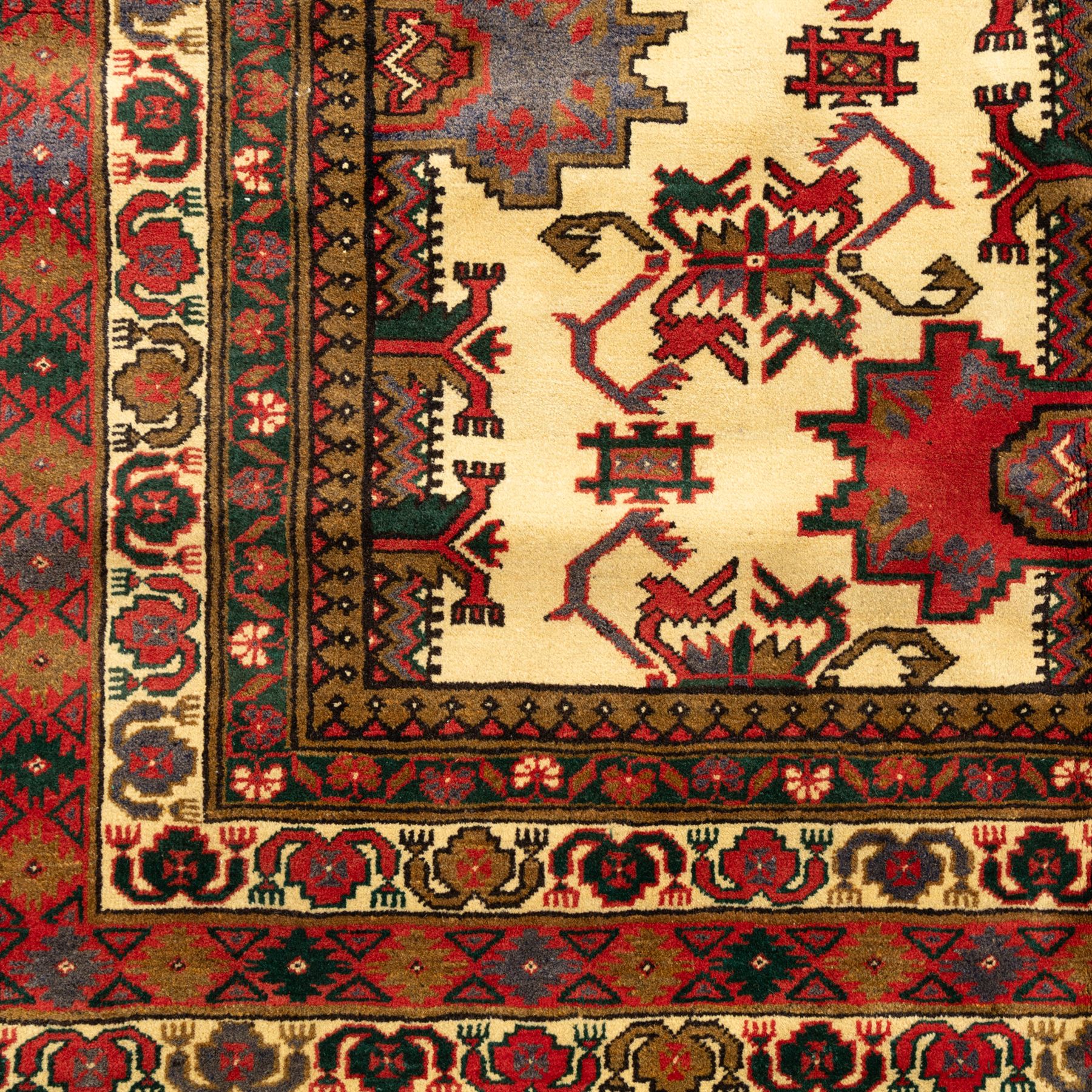North East Persian Gochan hand-knotted rug, ivory field decorated with a vertical column of stepped polygonal medallions flanked by stylized geometric floral motifs enclosed by multiple borders incorporating rosette and reciprocal devices, in a palette of madder red, indigo, olive green, and aubergine, with cotton fringe ends  