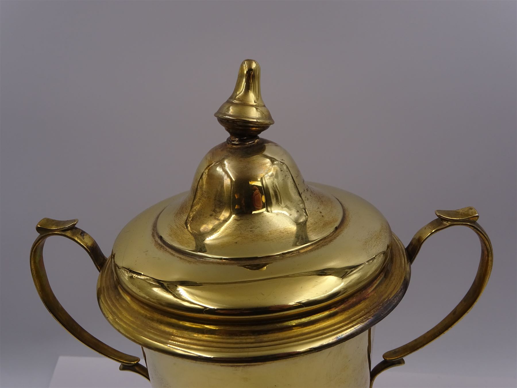 Edwardian silver-gilt twin handled trophy cup and cover, with two curved handles, the domed cover with urn finial, upon domed stepped foot and cylindrical mahogany base with applied plaque, hallmarked Skinner & Co, London 1908, total H29.7cm