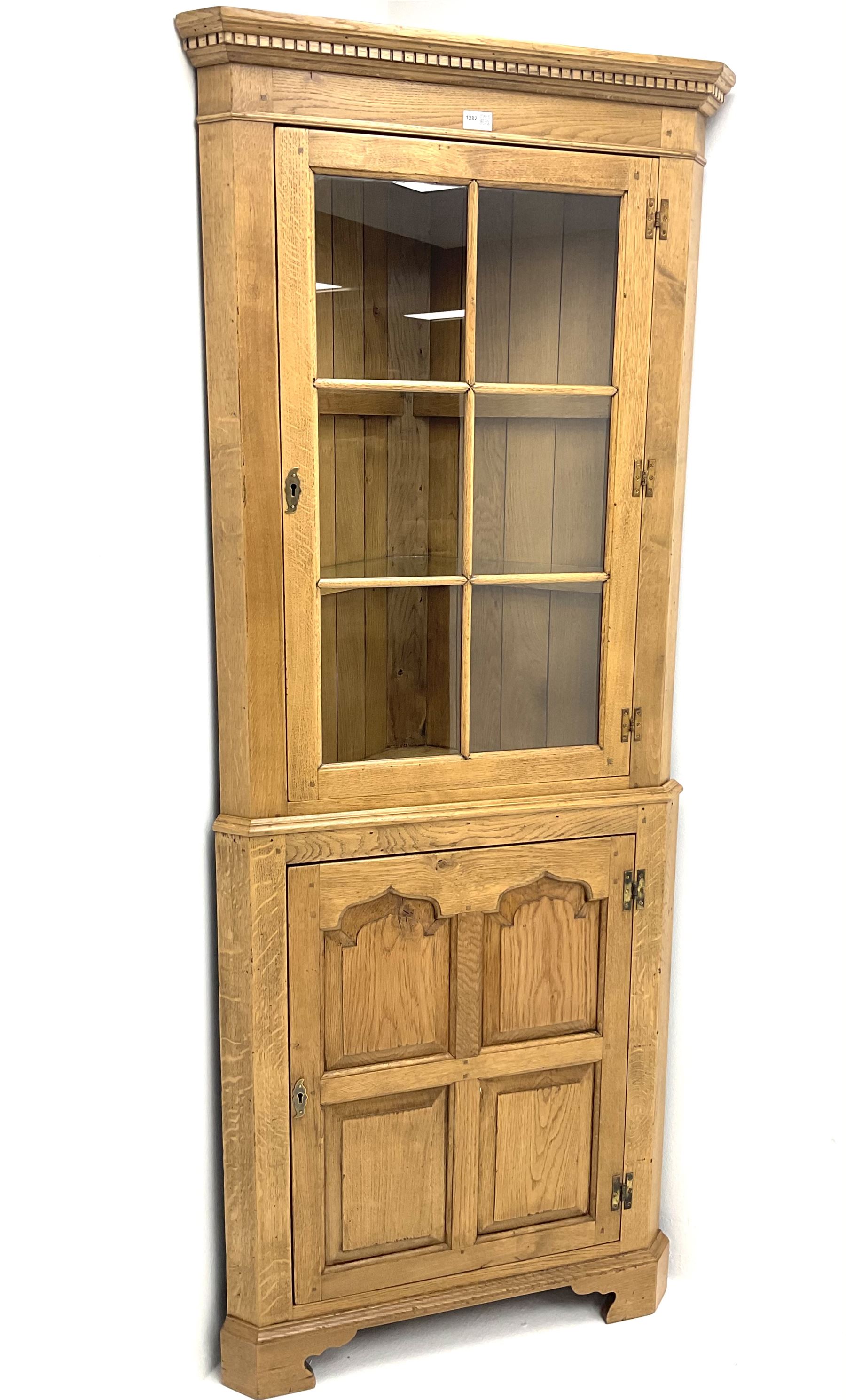 Oak corner cabinet, projecting cornice, dentil frieze, single glazed door enclosing two glass shelves above bottom unit, single fielded door enclosing fitted interior 