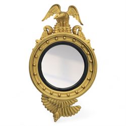 Early 20th-century Regency-style giltwood convex mirror, circular plate within a ball-mounted frame surmounted by an eagle cresting and flanked with scrolls, apron carved with foliate decoration 