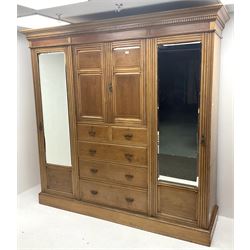 Edwardian walnut and ash triple combination wardrobe,  two bevel edge cupboard doors flanking two short and three graduating drawers and two cupboard doors enclosing three linen slides, platform base