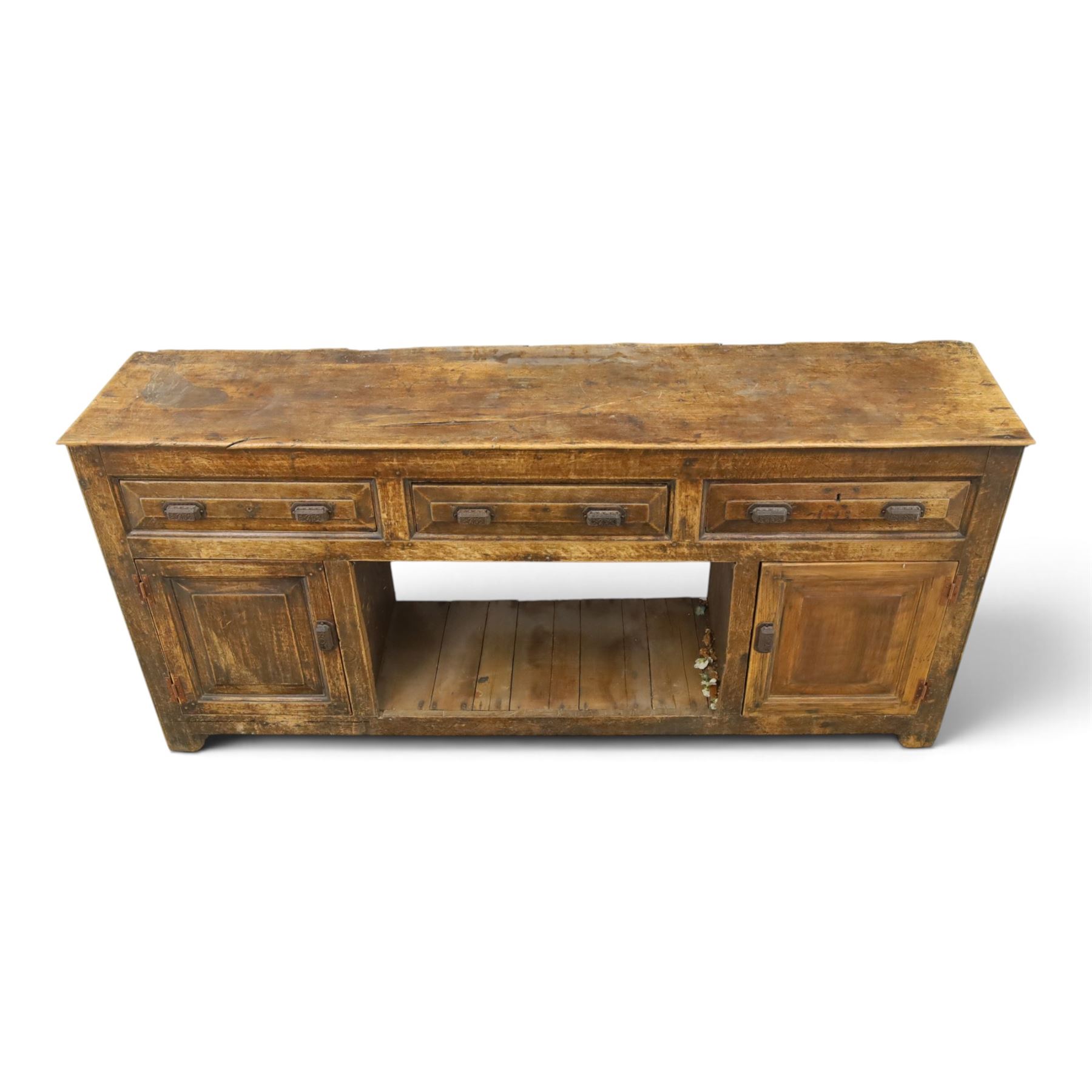 18th century rustic oak dresser base, with fielded panels and iron cup handles with embossed greek key and foliate detail, three short drawers above and open recess flanked by two cupboard doors, raised on stile supports
