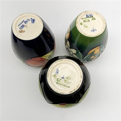 Three Moorcroft vases, the first of bulbous form tube line decorated with green apples against a dark blue glazed ground, the other examples of ovoid form, the first tube line decorated with plums against a dark blue glazed ground, the second decorated in the Passion Fruit pattern, each with marks beneath, tallest H14cm. 