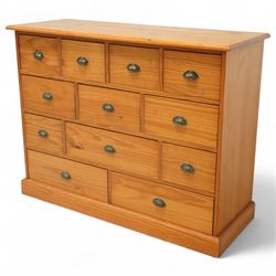 Late 20th century pine merchants chest, rectangular top over an arrangement of twelve small and four larger drawers, each with recessed panel facias and brass cup handles, plinth base