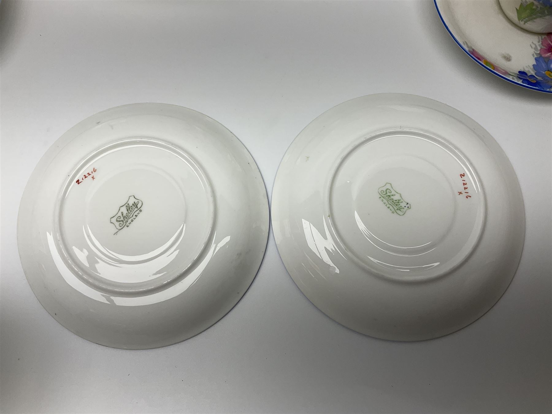 Shelley Strand shaped tea wares, decorated with blue and pink daisies upon a white ground, comprising four teacups, four saucers, three tea plates, milk jug, sugar bowl and cake plate, all with printed green mark beneath and painted pattern no 12216