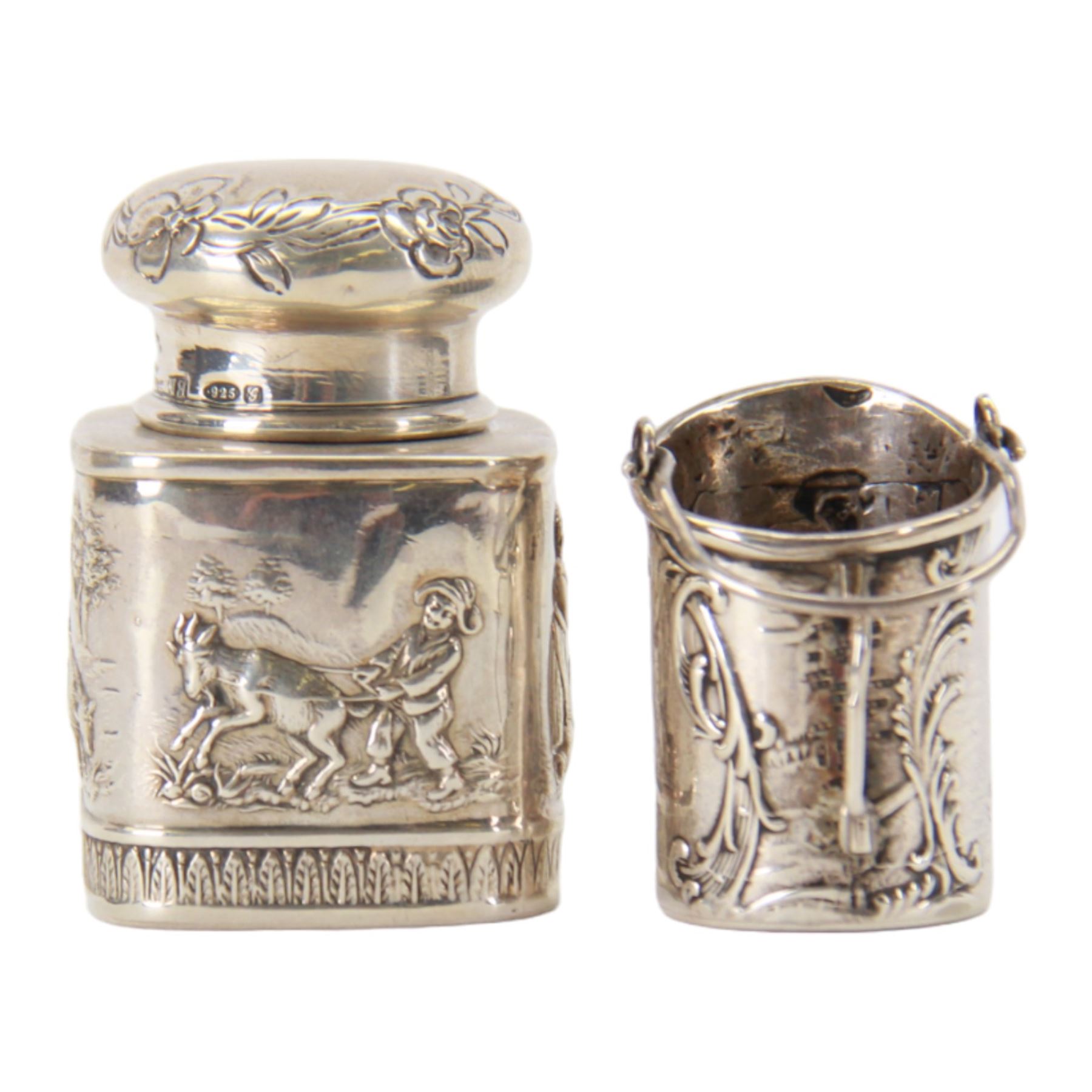 Late 19th century German Hanau silver miniature novelty scuttle, of cylindrical form with side handle and swing handle, the body impressed with figural genre scene, with Hanau marks for Karl Kurz, and hallmarked Samuel Boyce, Chester 1902, with 'F' foreign import mark, not including handle H3.5cm, together with a late 19th century German Hanau silver miniature novelty tea caddy, of rounded cube form, the body impressed with figures at work in a countryside setting, with Hanau marks for Neresheimer & Sohne, and hallmarked B Muller & Son, Chester import 1907, and marked 925, H5cm