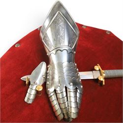 Three replica gauntlets, each housed upon a red wall shield, two with daggers, the third with a sword, largest H102cm