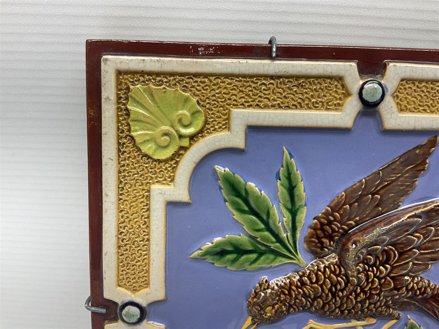 19th century Minton & Co majolica tile, decorated in relief with a bird upon a fruiting branch against a blue ground, with textured ochre border and anthemion to each corner, impressed mark verso, H19.7cm
