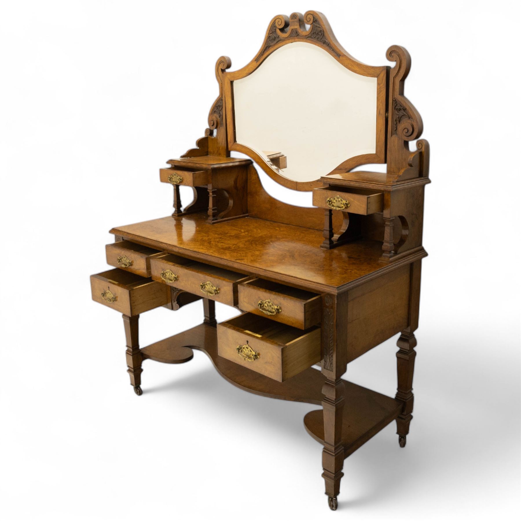 Late Victorian burr walnut veneer dressing table, the arched swing mirror surmounted by pierced scroll cresting, flanked by twin drawers on turned columns, over moulded rectangular top with five drawer arrangement, on block supports with shaped undertier