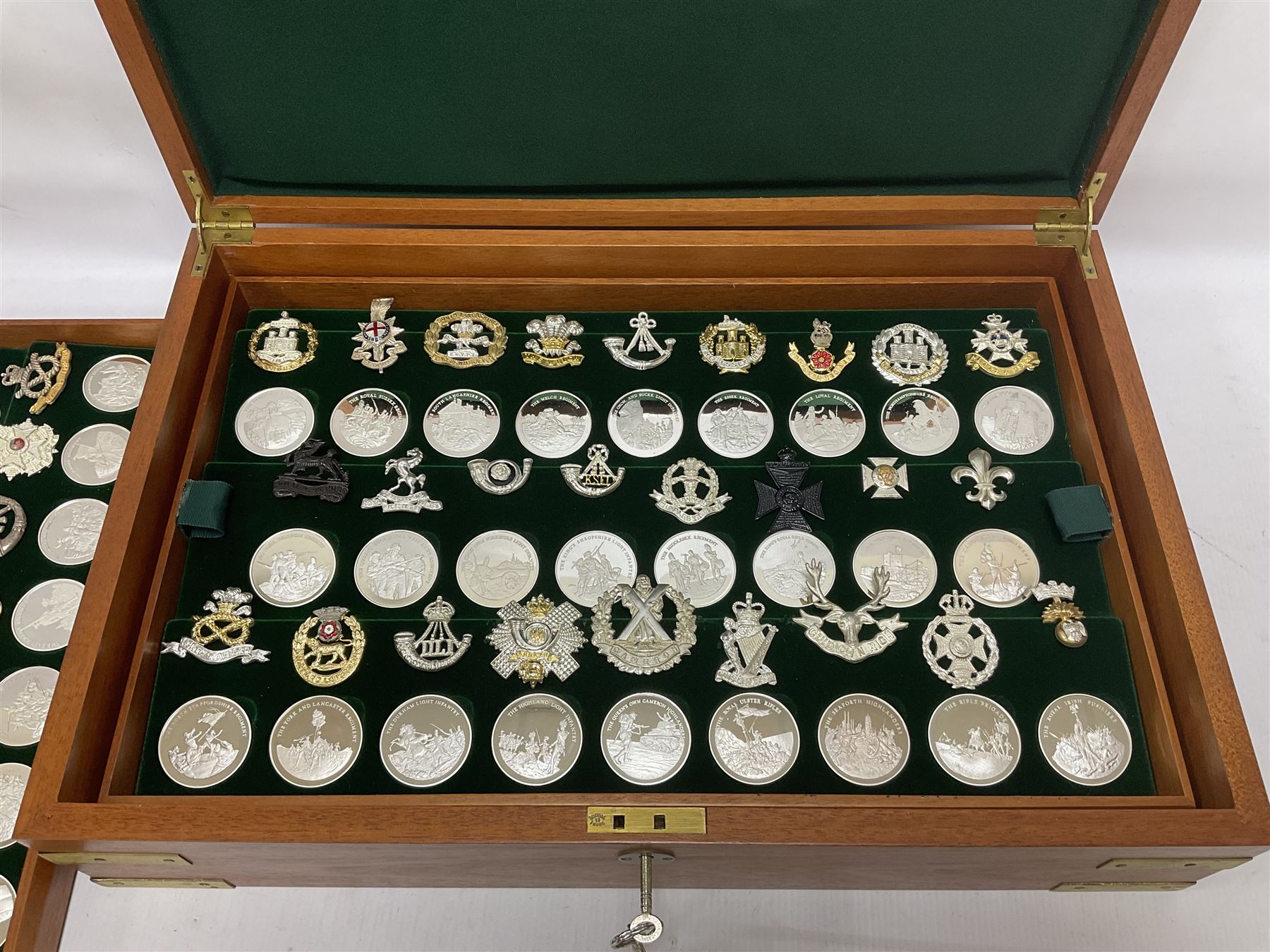 Great British Regiments, 1977, set of fifty two frosted silver medals by the Birmingham Mint, each bearing the name of a regiment with a depiction of an action on the obverse and further details on the reverse, all hallmarked Birmingham Mint, assay offices and dates; together with 52 base metal copy cap badges for each regiment, all housed and mounted on two trays and contained within a wooden presentation case, with brass plaque and fittings, lock and key, with a certificate of authenticity 