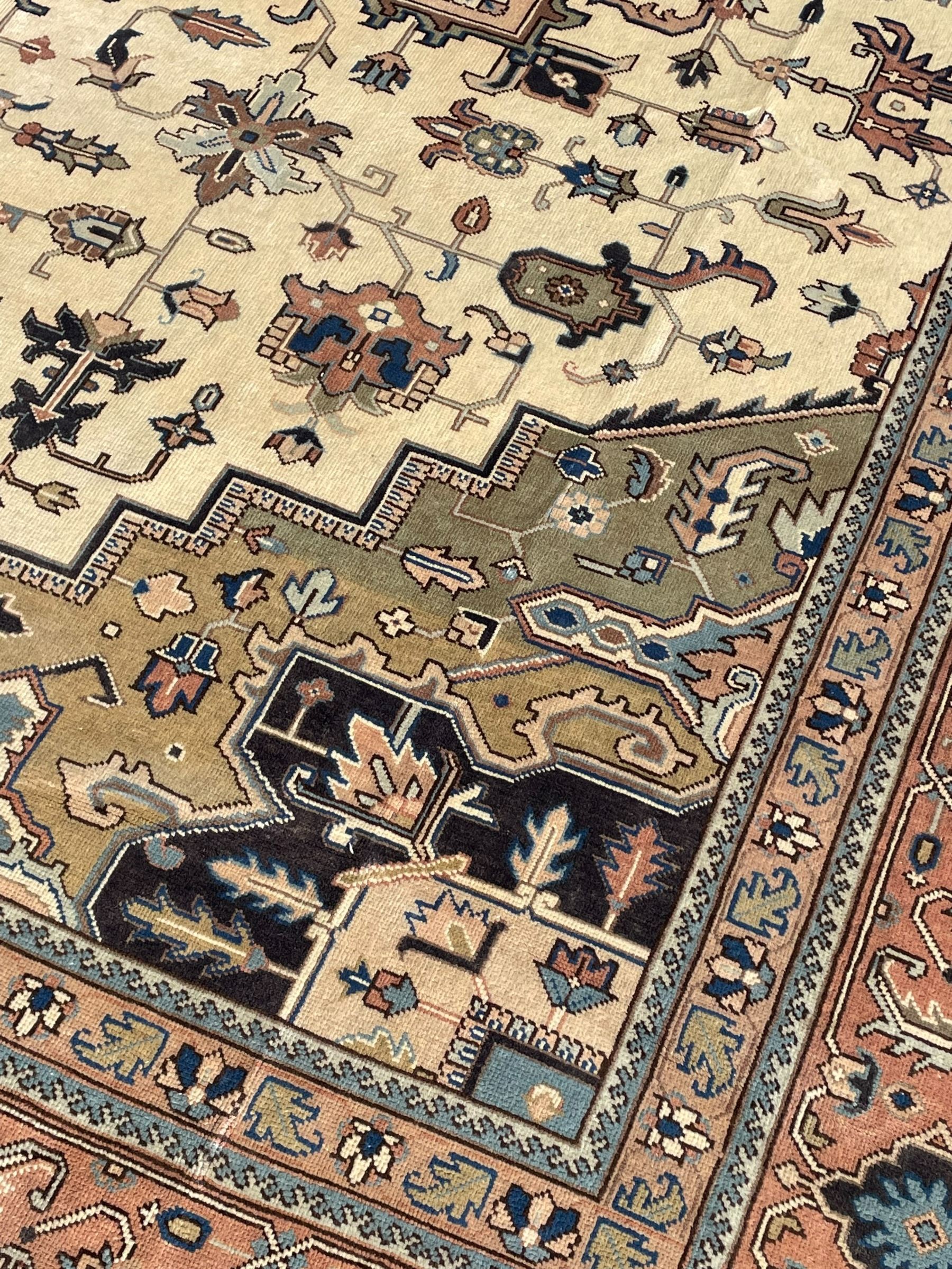 Persian Heriz pale olive and ivory ground carpet, large quatrefoil medallion with palmettes, the surrounding field decorated with trailing leafy branches and stylised plant motifs, peach ground borders with overall floral pattern, within guard stripes 