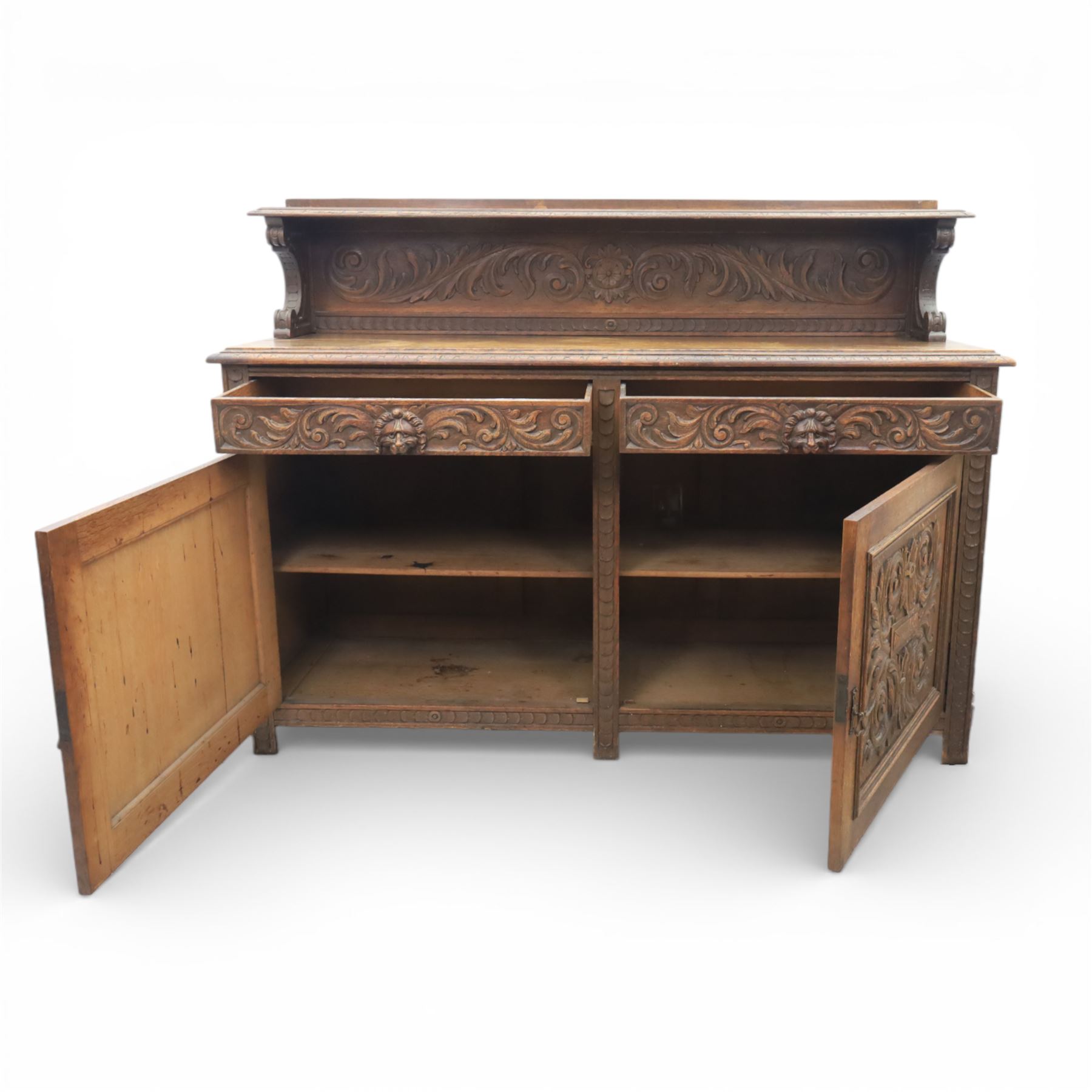 Victorian carved oak sideboard, the rectangular top with raised back carved with foliate scrolls and scroll end supports, upon a base with rectangular top with moulded edge, pair of drawers with conforming carved decoration and mask handles, and pair of carved cupboard doors, upon short stile type feet H101.5cm W183cm D54cm 