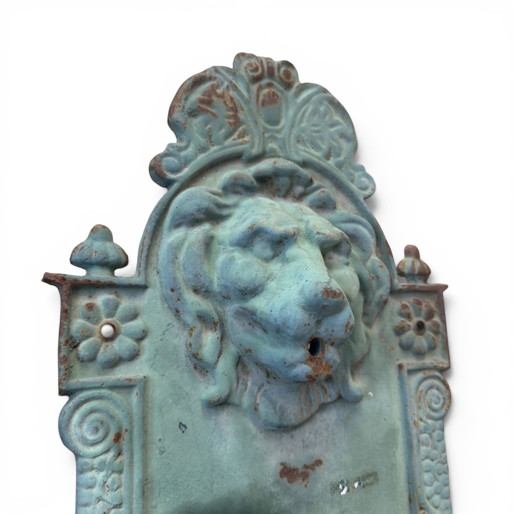 Antique cast iron wall fountain, cartouche cresting rail over a lion mask spout, with scroll and floral decoration over a scalloped basin, in rustic turquoise painted finish with rusted patina