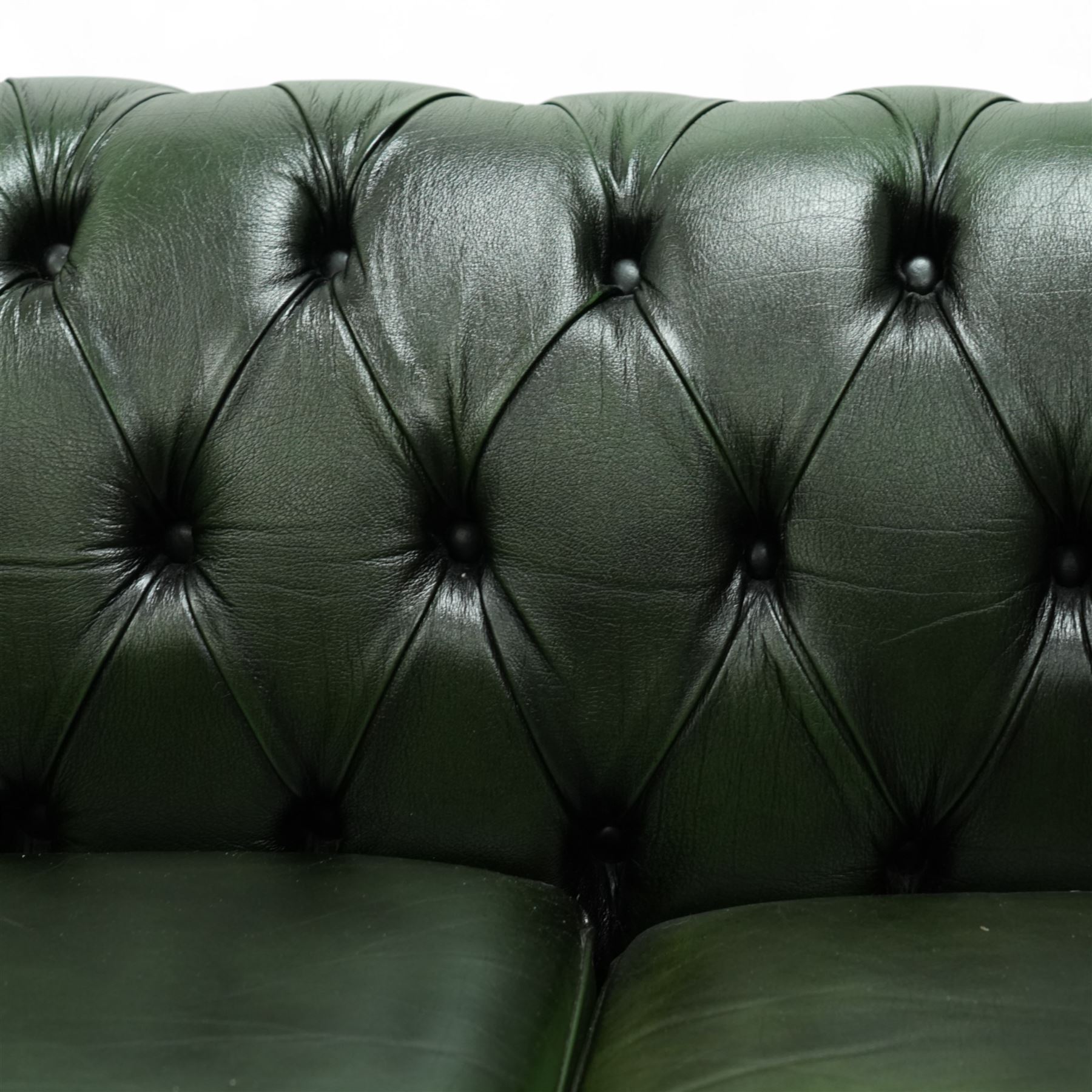 Late 20th century chesterfield style sofa upholstered in green leather, with deep buttoned back and arms above three loose cushions, continuous scroll arms and front, on concealed block feet