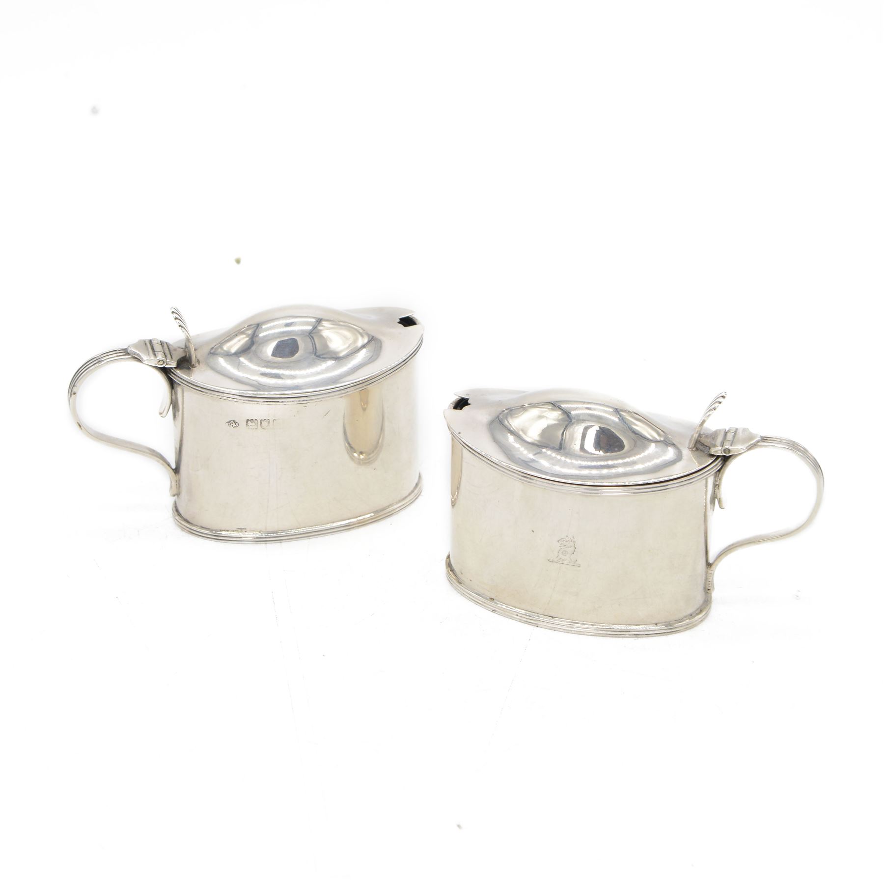 Pair of Edwardian silver mustard pots, of oval form with reed borders and palmette thumb pieces to hinged covers, opening to reveal blue glass liners, hallmarked William Hutton & Sons Ltd, London 1905, H7.5cm