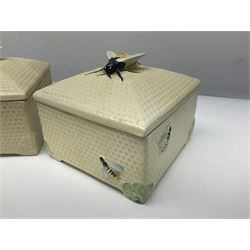 Four square honey boxes with lids,  each decorated with honeycomb pattern and finished with a bee finial
