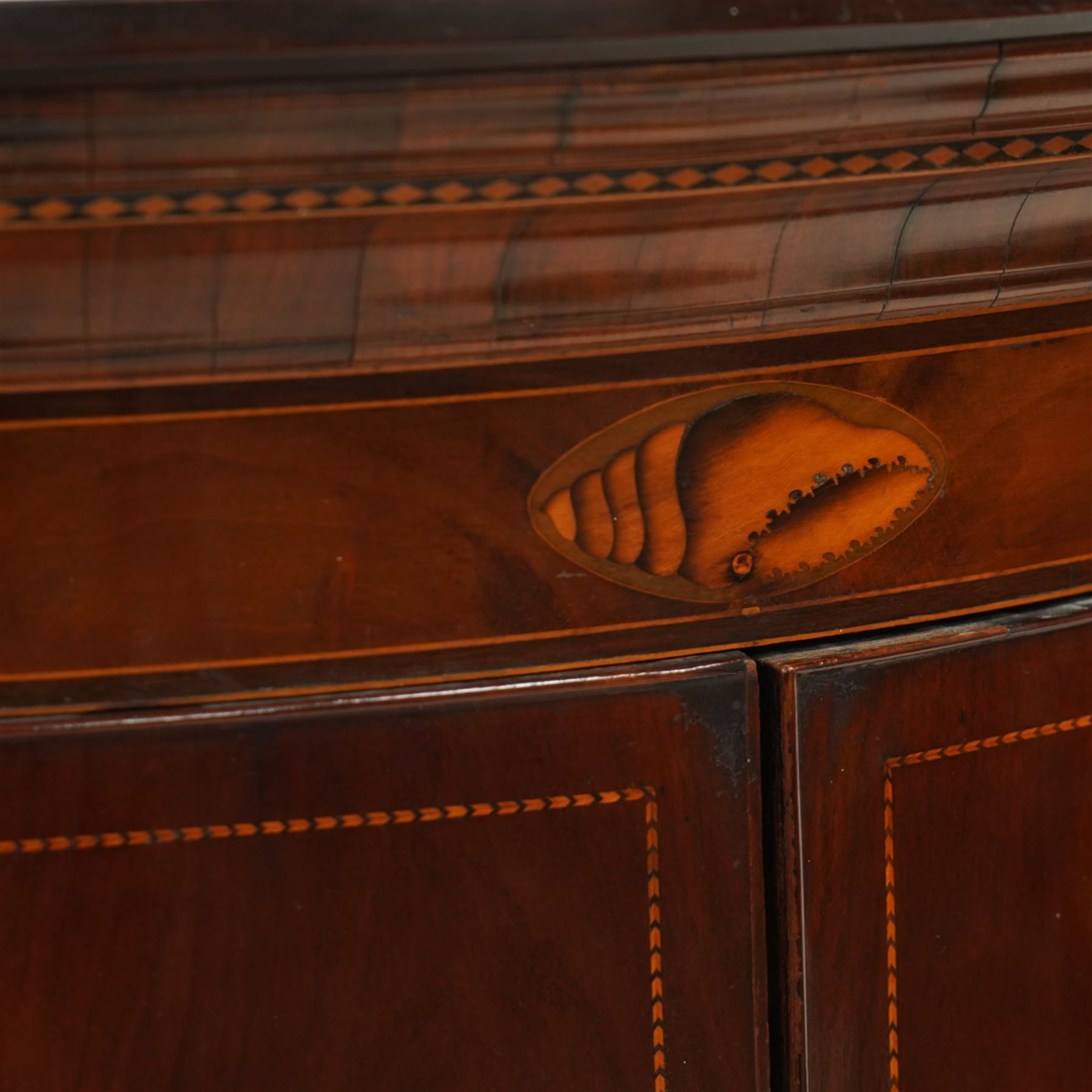 George III inlaid mahogany cylinder corner cupboard, projecting moulded cornice over figured frieze inlaid with shell motifs, two doors with checkered stringing enclosing three shelves, circa 1800