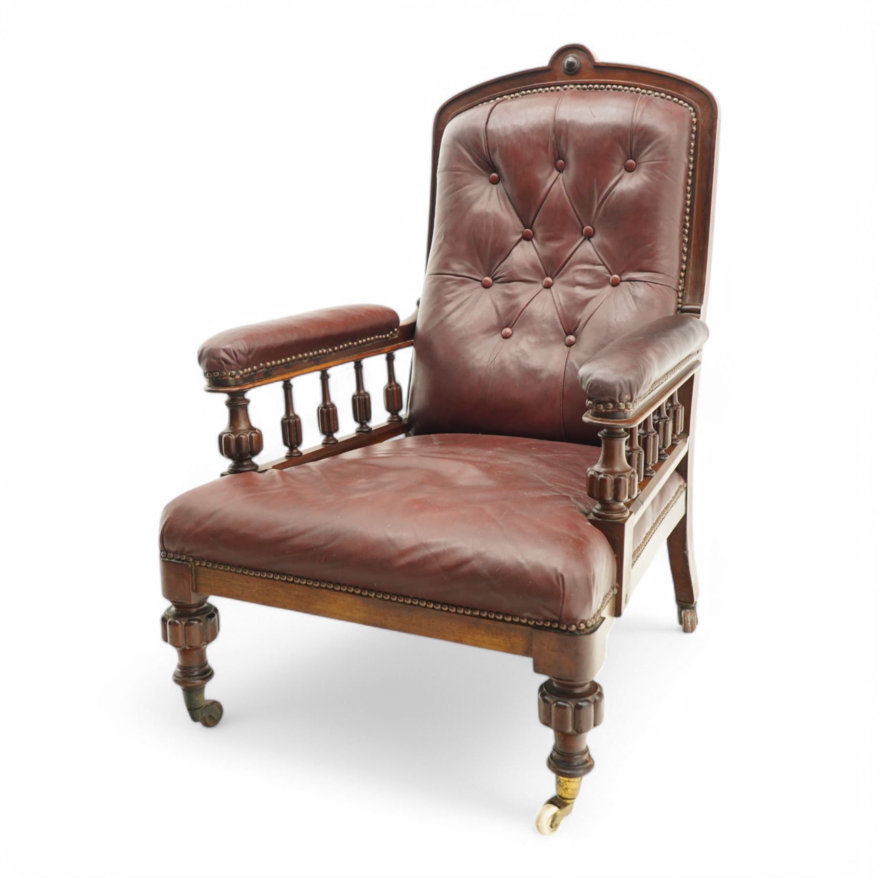 Late Victorian mahogany open armchair, arched cresting rail decorated with turned roundel, upholstered in buttoned burgundy leather, the upholstered arms on turned and lobe carved balustrade, turned and lobe carved front feet with brass and ceramic castors 