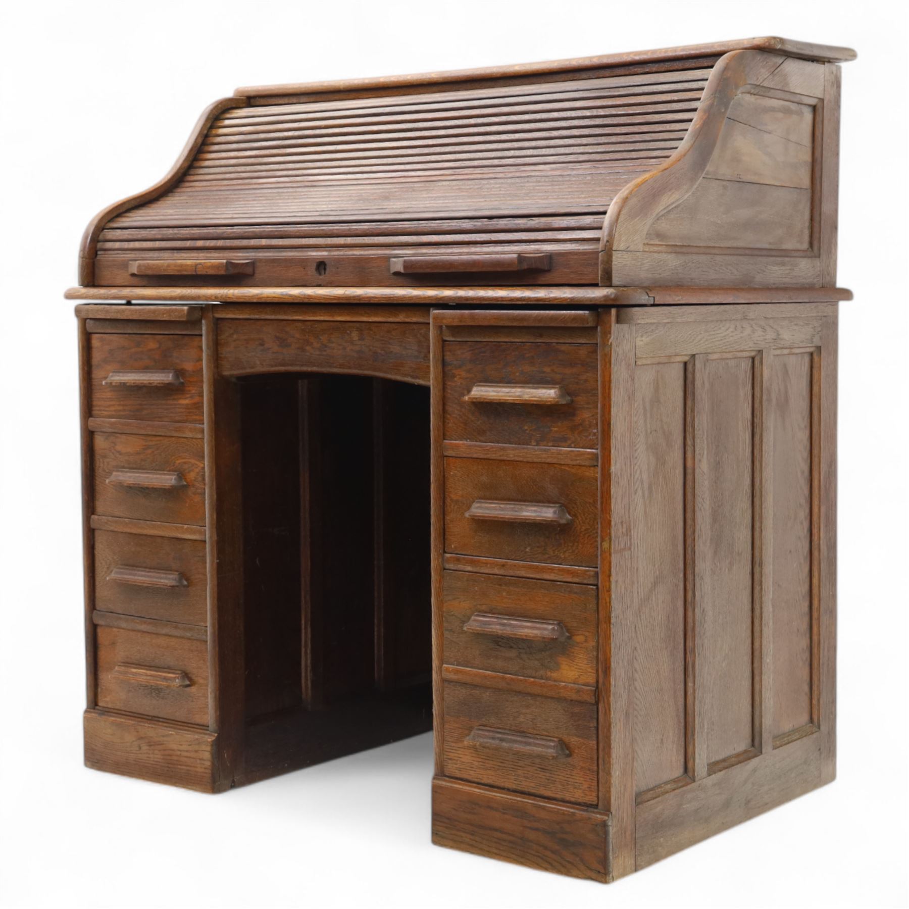 Early 20th-century oak roll-top desk with tambour shutter, enclosing a fitted interior of pigeon holes and small drawers, and pedestal base fitted with nine drawers with moulded handles, raised on plinth base 