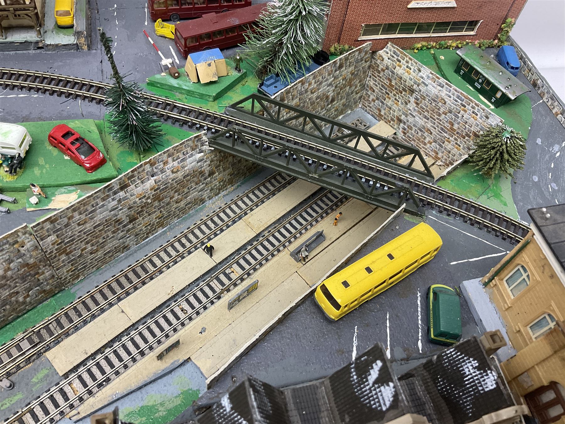 Table top 'N' gauge continental scenic layout as a split level town with various loops of track, station with numerous platforms, engine shed, assorted buildings, roads with motor vehicles and figures, tunnels, trees, river with bridge, tram depot etc 122 x 52cm