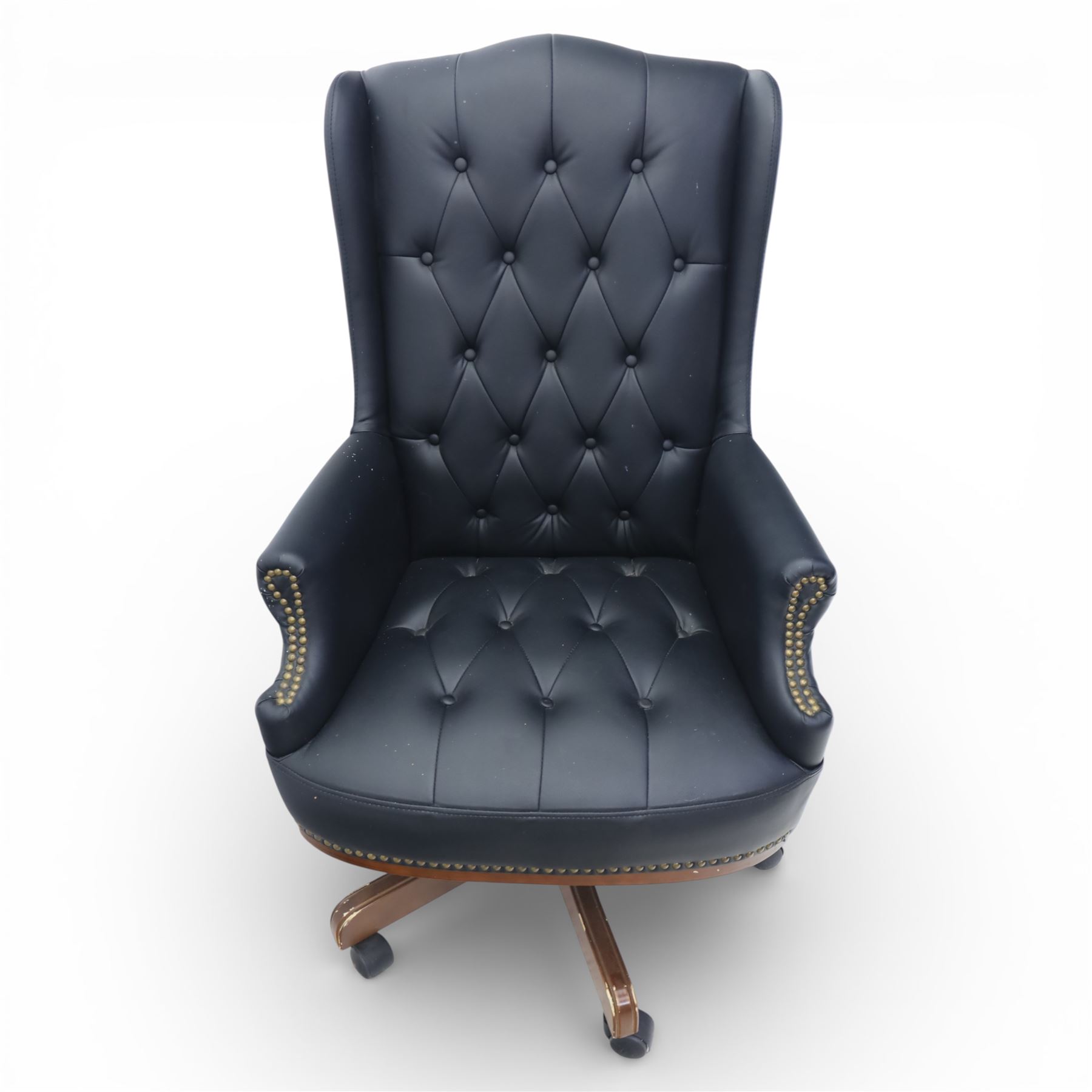 Chesterfield style desk chair upholstered in black, brass studded trim with tall button backed seat, with faux wooden base raised upon castors