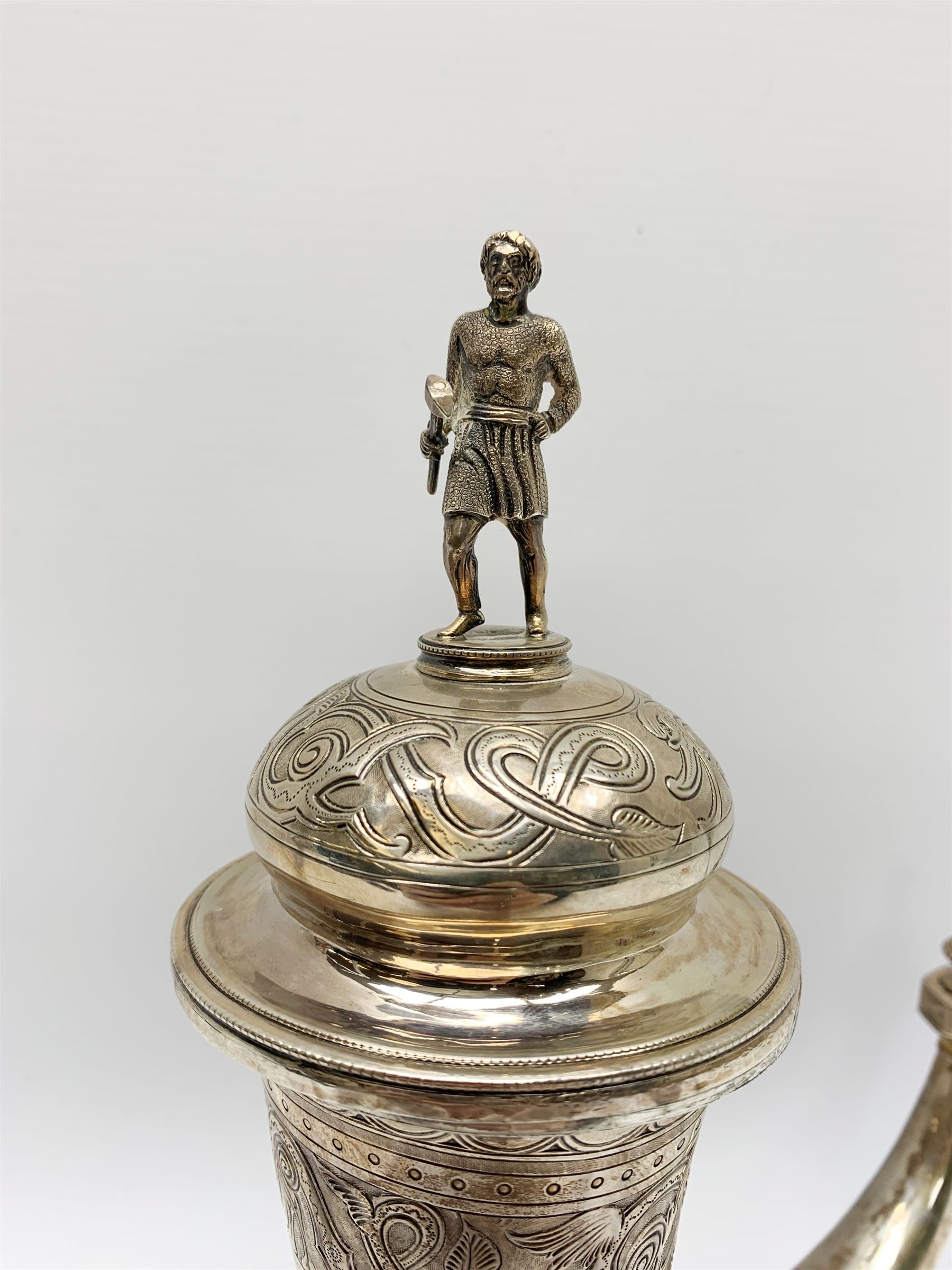 Late 19th century Danish silver drinking horn and cover, the body with hexagonal and beaded finial, raised upon two talon feet and further scroll foot, chased with scrolling foliate and zoomorphic bands, the detachable domed cover with conforming decoration surmounted by a figure holding a hammer, the cover interior impressed with maker's mark (partly worn and indistinct), alongside Danish Three Towers mark for 1881, with the Assay Master mark for Simon Groth (1863-1904), H23.5cm, weight 14.75 ozt (459 grams)

