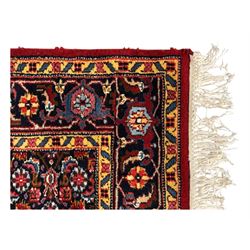 Persian crimson ground rug, central light blue lozenge medallion with floral motifs, the densely decorated crimson field filled with repeating flower heads and trailing leafy vines, the black and red border with interlacing foliate patterns and floral cartouches, surrounded by guard stripes