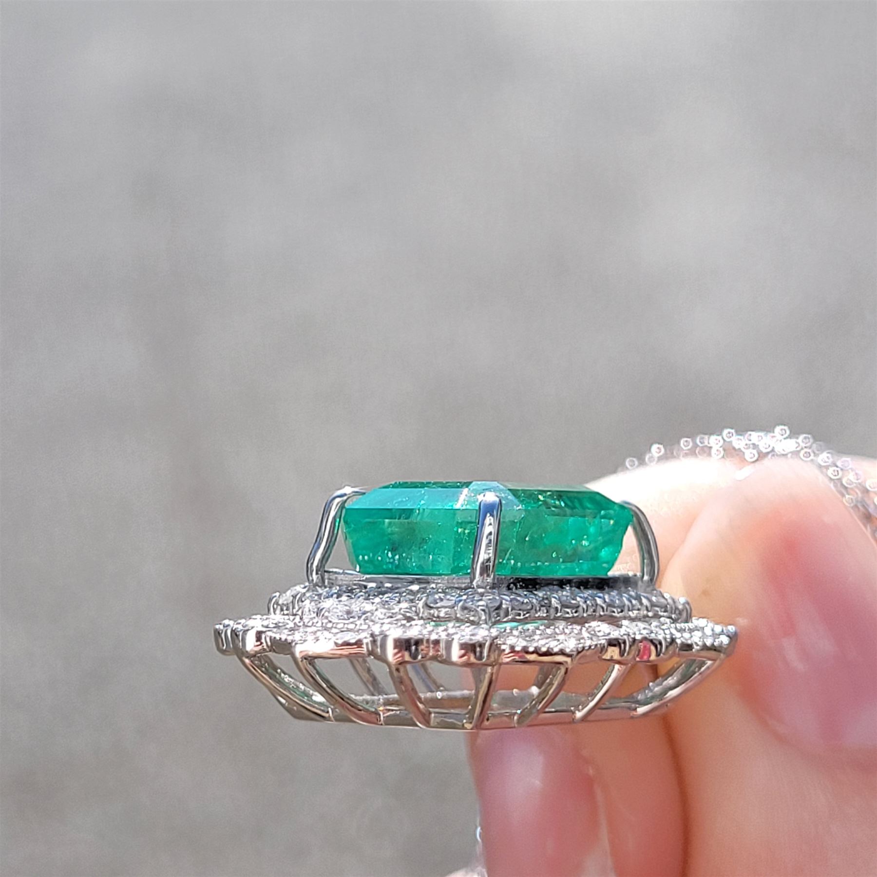 Platinum Colombian emerald and diamond pendant necklace, single octagonal cut emerald of 7.38 carat, surrounded by round cut diamonds in a fancy milgrain pierced design setting, stamped Pt 950, on a trace link chain necklace, total diamond weight 1.14 carat, with GCS certificate