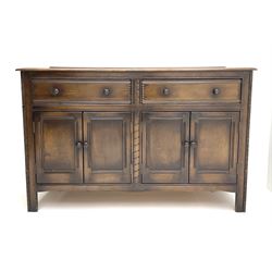 Ercol elm sideboard, fitted with two long drawers above two double panelled cupboard doors enclosing shelving, raised on carved stile supports