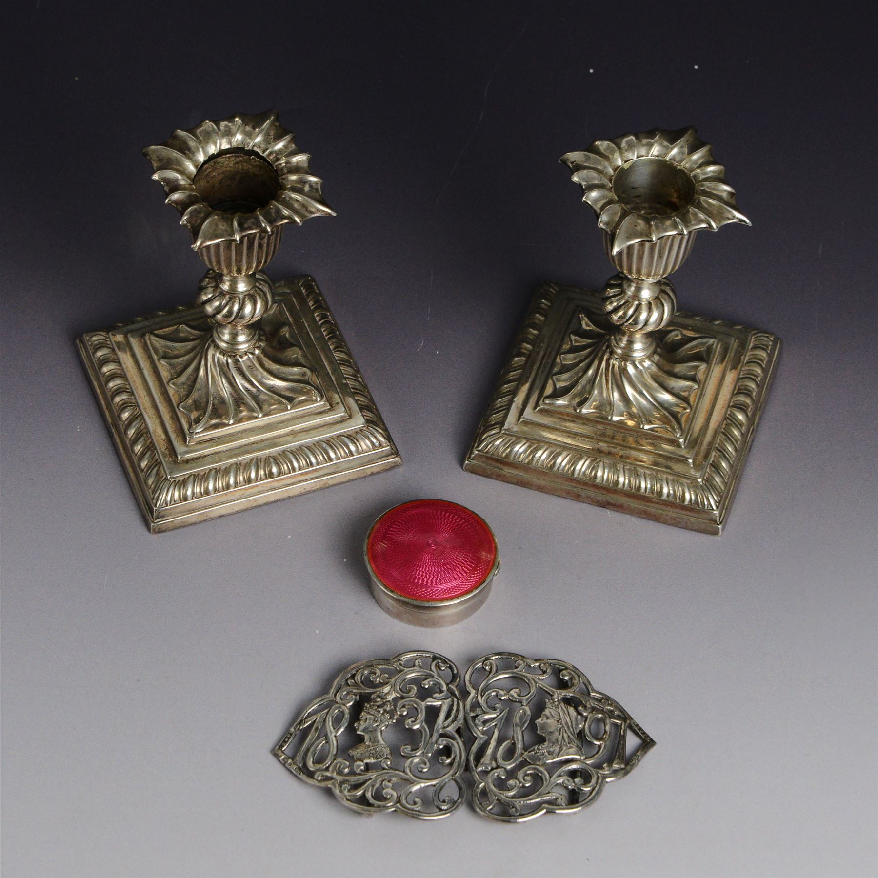 Early 20th century silver pill box, of circular form with pink guilloche enamel lid, hallmarked Deakin & Francis, Deakin & Francis Ltd, Birmingham 1911, together with a commemorative Queen Victoria belt buckle, and a pair of late Victorian dwarf candlesticks with weighted bases, all hallmarked, box D4cm